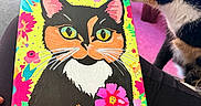 Croia is registered to the contest to win money with this photo: animal, art, calico_cat, canvas, cat, closeup, colorful, cozy, curious, decor, flowers, indoor, painting, pet, pink, purple, sniffing, table, vibrant, wooden