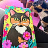 cat, calico_cat, painting, colorful, flowers, art, canvas, indoor, table, pink, purple, wooden, curious, sniffing, animal, pet, closeup, vibrant, cozy, decor