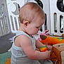 arm, baby, bookshelf, child, colorful, floor_mat, focus, furniture, head, indoor, leg, onesie, person, playpen, plush_toy, room, sitting, skin, toddler, toy