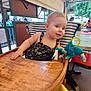 baby, cafe, child, clothing, cute, daylight, greenery, happy, high_chair, outdoor, people, person, playful, plush_toy, relaxing, seat, smiling, striped_cushion, table, wooden_furniture