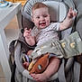 baby, baby_seat, blanket, child, clothing, face, floor, foot, furniture, hand, happy, home, indoor, infant, person, smiling, table, television, toy, wooden_door