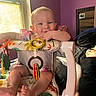 Luna is registered to the contest to win money with this photo: baby, baby_seat, bedroom, child, clothing, colorful, cute, face, foot, furniture, hand, happy, indoor, infant, person, playful, purple_wall, smiling, toys, window