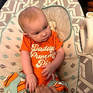 Luna is registered to the contest to win money with this photo: baby, baby_seat, child, comfort, curious, cute, face, hand, head, home, indoor, infant, onesie, orange_clothing, patterned_fabric, person, sitting, small_hands, soft_toys, wooden_furniture
