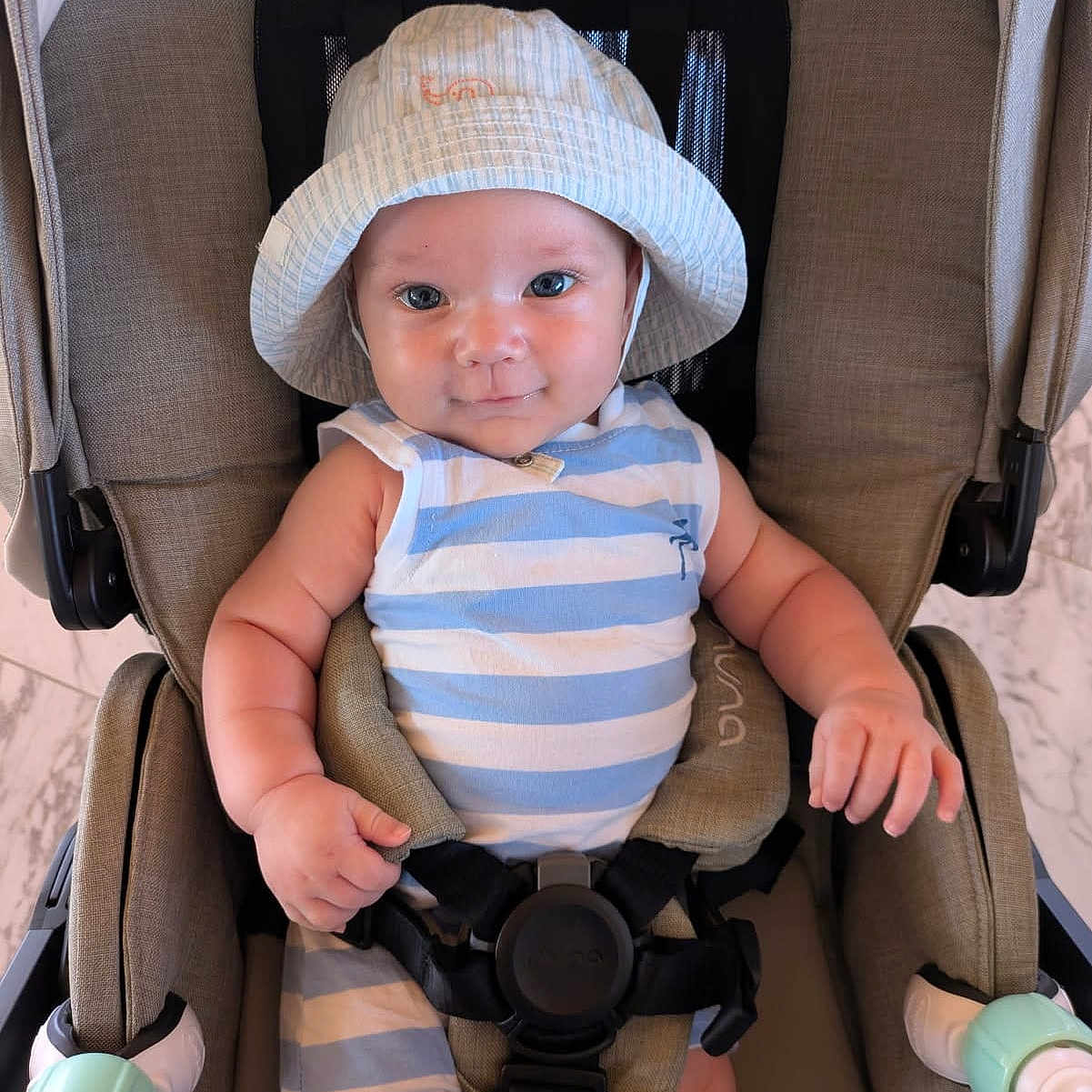 Loukian a rejoint le concours — aidez-le/la à gagner de superbes lots ! arms, baby, blue, child, comfort, cute, face, hands, hat, indoor, infant, person, portrait, seatbelt, sitting, smile, striped_clothing, stroller, white, young