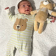 Jayden is registered to the contest to win money with this photo: baby, infant, onesie, striped_clothing, bear_face, plush_toy, teddy_bear, blanket, soft_texture, lying_down, cute, child, sleepwear, smiling, indoor, cozy, comfort, person, portrait, adorable