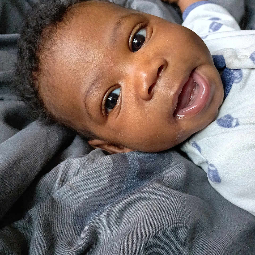 Rae'Mahn Barbin is registered to the contest to win money with this photo: baby, blanket, child, closeup, clothing, curly_hair, cute, expression, eyes, fabric, face, feet, happy, indoors, infant, lying_down, person, portrait, skin, smile
