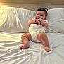 baby, infant, bed, white_clothing, smile, happy, chubby, hands, feet, pillow, sheet, indoor, light, wooden_headboard, caucasian, cute, sitting, toddler, skin, hair