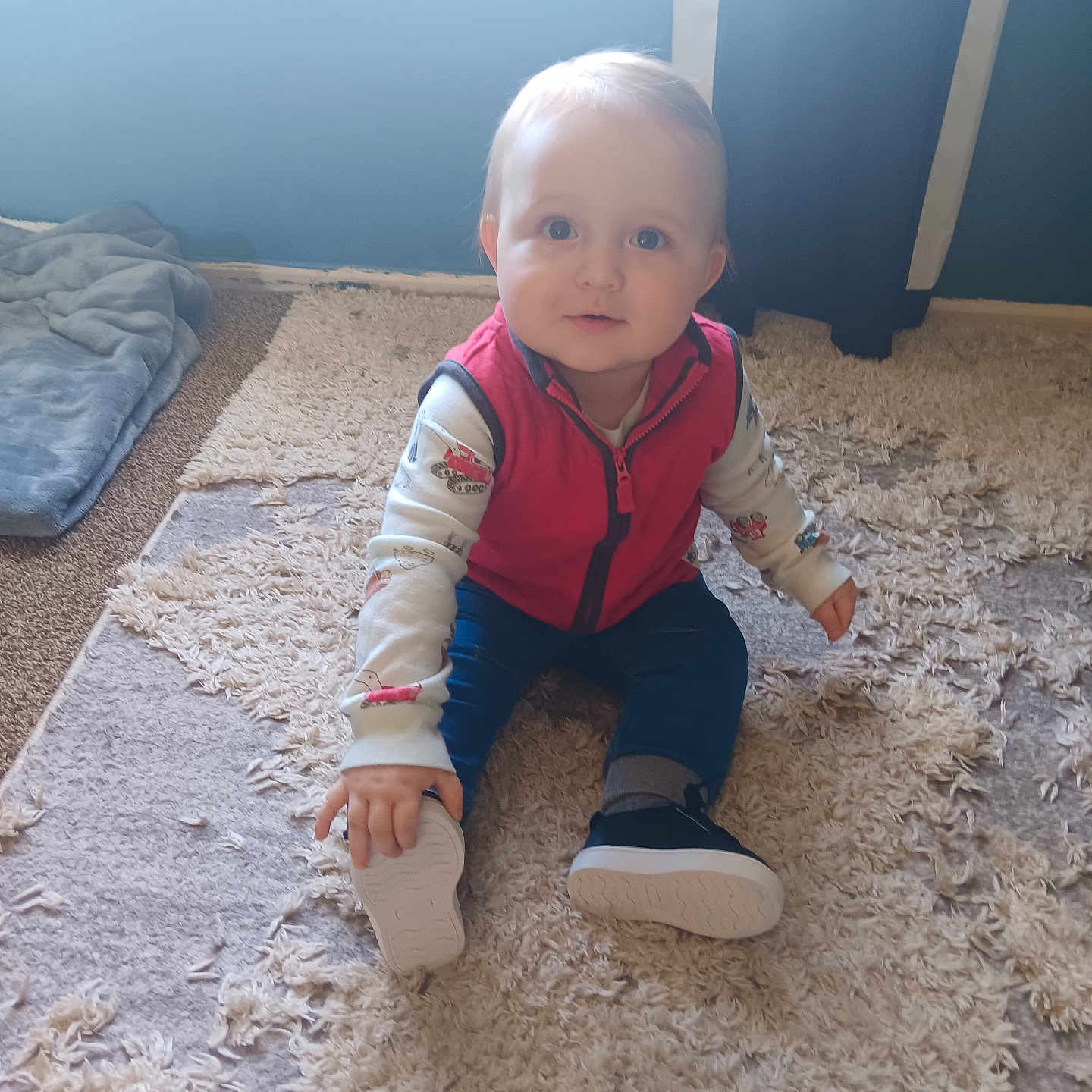 Elijah joined the competition — help win amazing prizes! baby, blue_wall, carpet, child, clothing, curtain, floor, floor_covering, hand, indoor, long_sleeve, looking, person, portrait, rug, shoe, sitting, soft_light, vest, window
