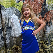 Remi is registered to the contest to win money with this photo: child, girl, cheerleader, pom_pom, blue_uniform, smile, long_hair, standing, hand_on_hip, indoor, horse_backdrop, cheerleading, portrait, yellow_trim, sportswear, confident, happy, background, floor, team_spirit
