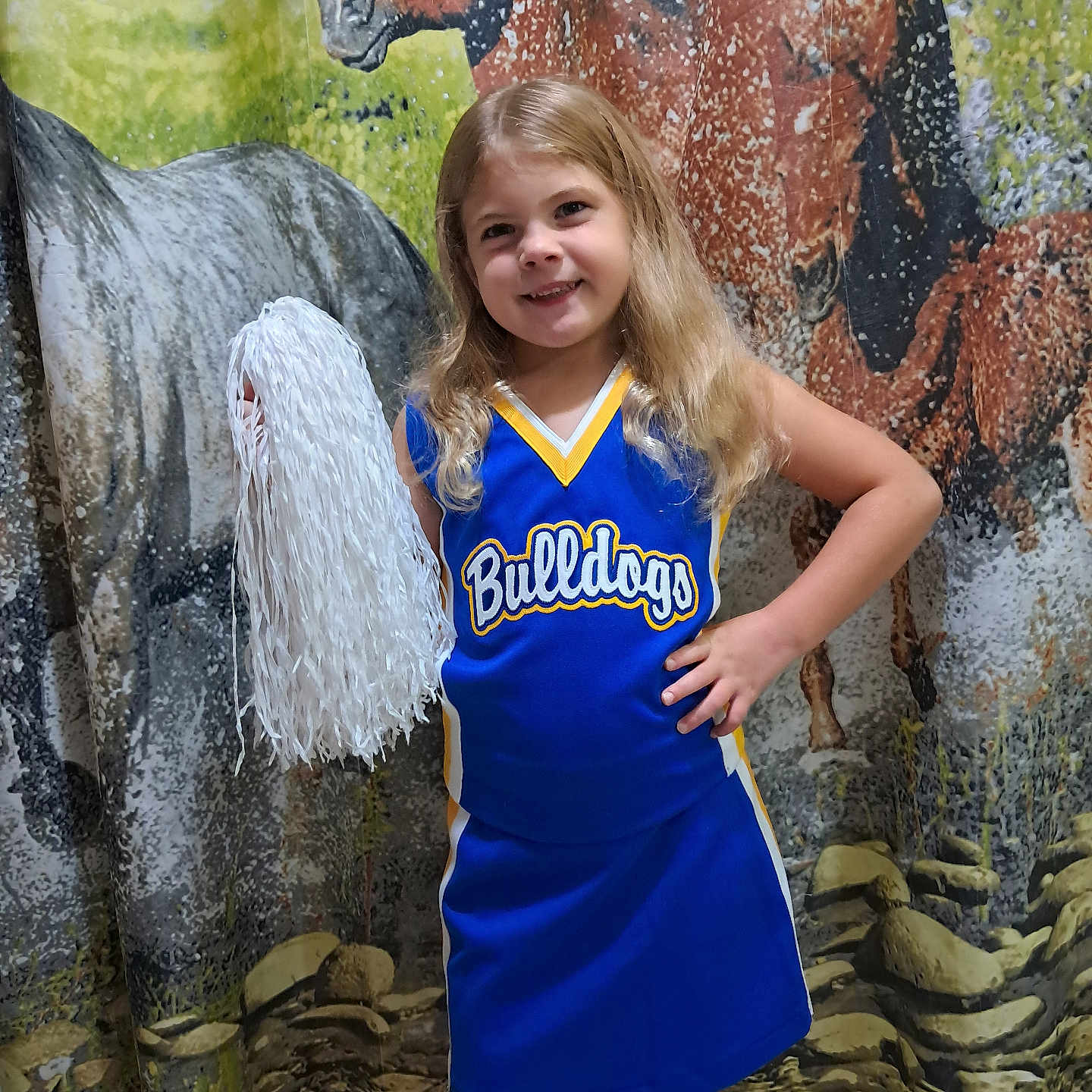 Remi is registered to the contest to win money with this photo: background, blue_uniform, cheerleader, cheerleading, child, confident, floor, girl, hand_on_hip, happy, horse_backdrop, indoor, long_hair, pom_pom, portrait, smile, sportswear, standing, team_spirit, yellow_trim