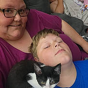 Zoey is registered to the contest to win money with this photo: woman, child, kitten, cat, couch, blanket, glasses, indoor, relaxing, sleeping, family, portrait, casual, home, smiling, blue_shirt, purple_shirt, black_and_white_cat, close_up, comfort