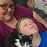 woman, child, kitten, cat, couch, blanket, glasses, indoor, relaxing, sleeping, family, portrait, casual, home, smiling, blue_shirt, purple_shirt, black_and_white_cat, close_up, comfort