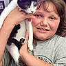 Zoey is registered to the contest to win money with this photo: child, cat, black_and_white_cat, pet, smiling, holding, indoor, portrait, young, cute, collar, bell, curious, happy, face, animal, person, casual_clothing, closeup, feline