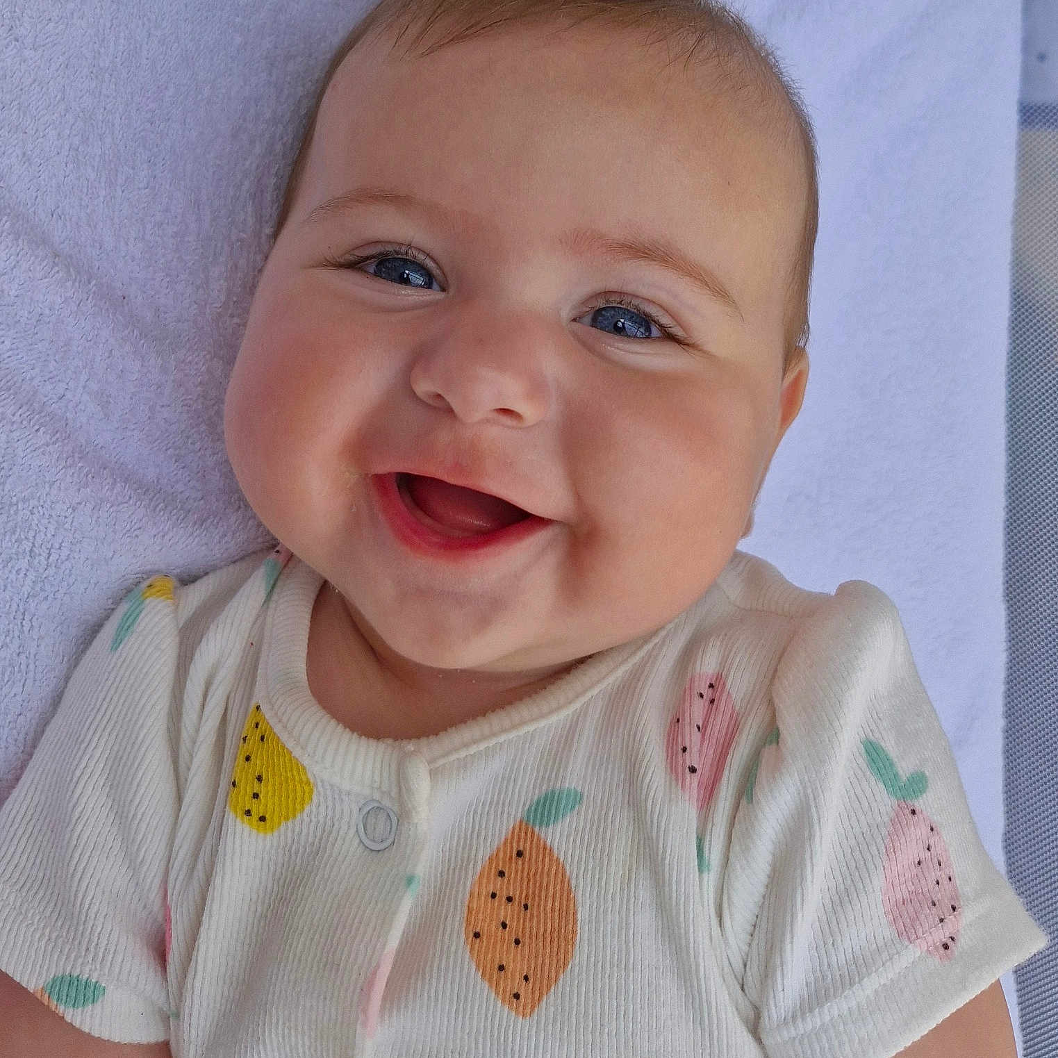 Cali participe au concours pour gagner de l'argent avec cette photo : baby, blue_eyes, cheeks, child, closeup, cute, expression, face, fruit_pattern, happy, indoors, infant, joy, lying_down, onesie, portrait, skin, smiling, towel, toy
