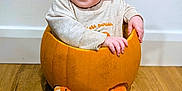Grace is registered to the contest to win money with this photo: baby, child, pumpkin, orange_hat, striped_leggings, smiling, happy, indoor, floor, wooden_floor, cute, portrait, hat, sitting, seasonal, fall, autumn, cozy, playful, infant