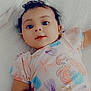 baby, infant, child, onesie, mermaid, hand, white_quilt, cute, lying_down, portrait, soft_lighting, indoor, smiling, curly_hair, playful, colorful_clothing, tender_moment, close_up, happy, skin