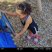 Ashanti is registered to the contest to win money with this photo: activity, black_outfit, casual_clothing, child, curly_hair, daylight, footwear, fun, outdoor, person, pink_sandals, play, playground, recreation, steering_wheel, summer, toddler, toy, wood_chips, young_child