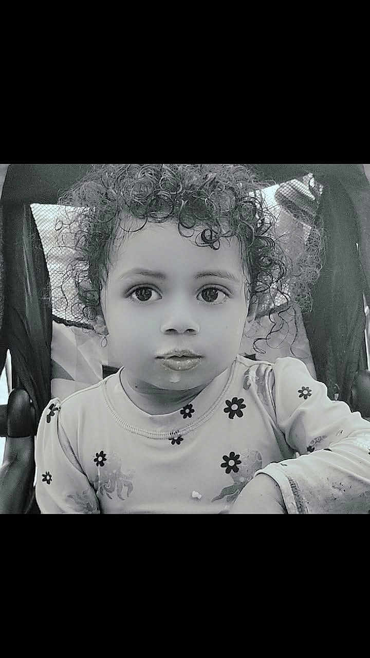 Ashanti is registered to the contest to win money with this photo: child, toddler, curly_hair, face, stroller, shirt, flower_pattern, food, expression, portrait, black_and_white, sitting, young_child, cute, eyes, mouth, clothing, indoor, baby, person