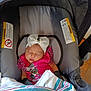 baby, sleeping, car_seat, headband, bow, pink_clothing, blanket, infant, child, indoor, warning_label, seat, resting, cute, newborn, toddler, face, person, comfort, child_safety