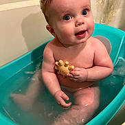 Cullen is registered to the contest to win money with this photo: baby, bathtub, water, toy, child, sitting, bath, happy, skin, face, expression, indoor, curly_hair, naked, toddler, blue, yellow, play, cute, infant