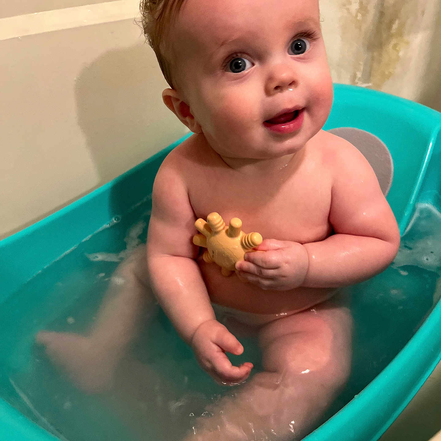 Cullen is registered to the contest to win money with this photo: baby, bathtub, water, toy, child, sitting, bath, happy, skin, face, expression, indoor, curly_hair, naked, toddler, blue, yellow, play, cute, infant