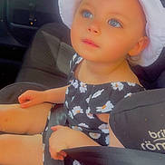 Esme is registered to the contest to win money with this photo: toddler, child, baby, car_seat, seatbelt, hat, white_hat, blue_eyes, floral_dress, black_dress, car_interior, seat, safety, portrait, cute, young_child, summer_clothing, sunhat, sitting, looking_up