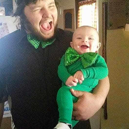 Micah is registered to the contest to win money with this photo: adult, baby, child, green_clothing, bow_tie, smiling, laughing, indoor, home, person, holding, joyful, casual, window, light, happy, family, portrait, celebration, fun