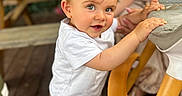 Sacha a rejoint le concours — aidez-le/la à gagner de superbes lots ! adult, bench, blurred_background, brown_pants, child, curious, face, flower, hair, hand, high_chair, indoor, light, person, smile, sneakers, toddler, white_tshirt, wooden_floor, wooden_furniture