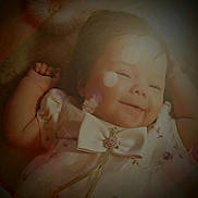 Olivia joined the competition — help win amazing prizes! baby, infant, child, smile, face, bow, dress, rose, floral_pattern, bokeh, lens_flare, soft_light, portrait, lying_down, hand, arm, cozy, fabric, blanket, adorable