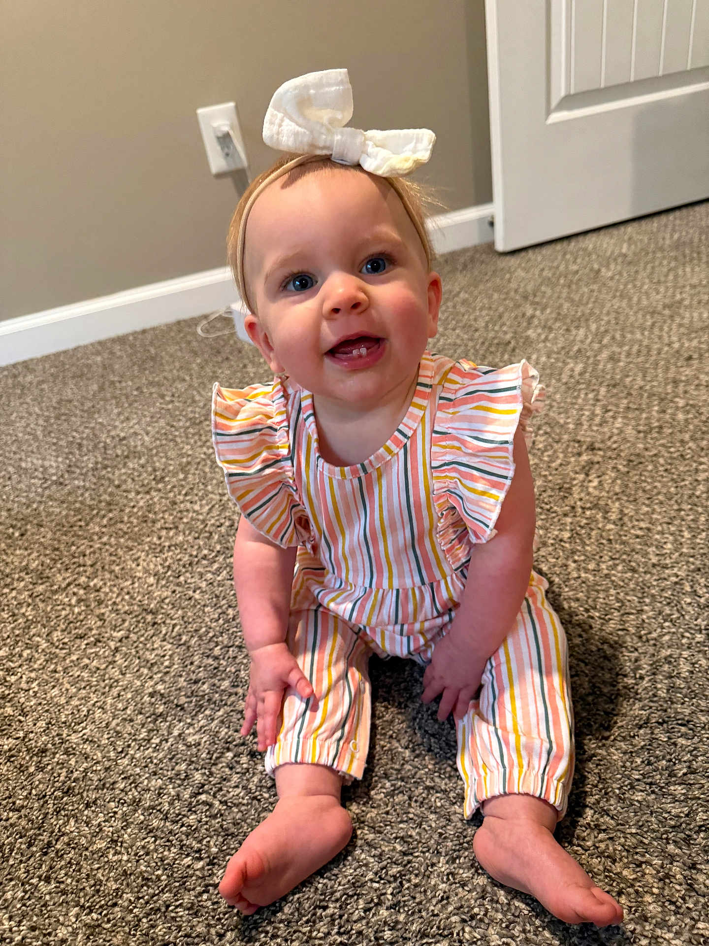 Morgan is registered to the contest to win money with this photo: baby, child, smiling, headband, bow, striped_clothing, carpet, indoor, floor, person, cute, happy, infant, sitting, toes, hand, face, young_child, room, door