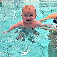Clément participe au concours pour gagner de l'argent avec cette photo : baby, infant, swimming_pool, water, smile, happy, splash, indoor_pool, tiles, yellow_slide, parent_hand, supporting_hand, portrait, cute, floating, bare_chest, legs, reflection, waves, turquoise