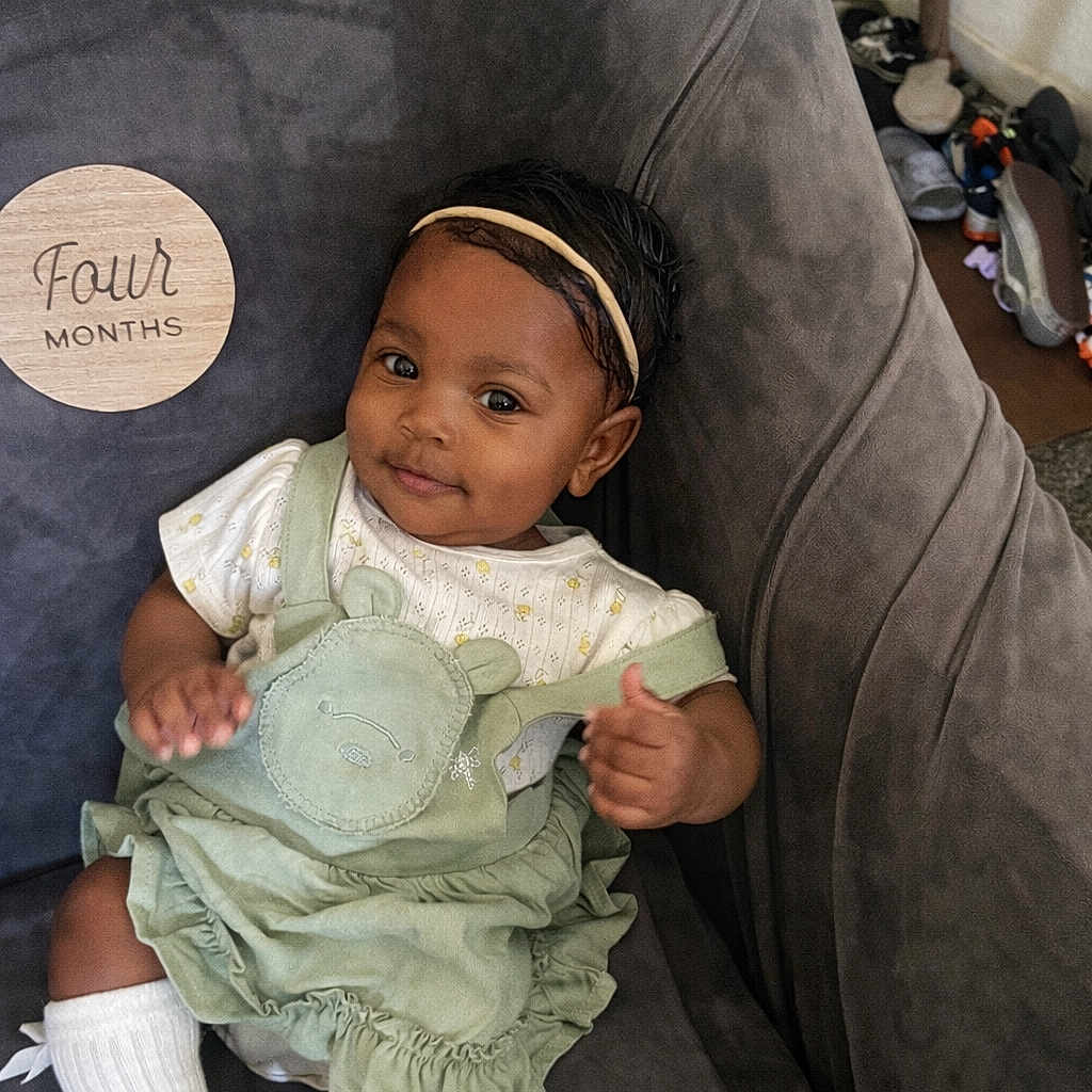 Freya Handy is registered to the contest to win money with this photo: baby, infant, child, smiling, headband, green_dress, socks, chair, plush, milestone, wooden_plaque, indoor, cute, portrait, person, happy, sitting, young_child, comfortable, home