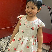 Fatma is registered to the contest to win money with this photo: child, toddler, dress, strawberry_print, smile, indoor, carpet, door, short_hair, cute, person, girl, patterned_floor, happy, standing, white_dress, red_door, floor, young_child, portrait