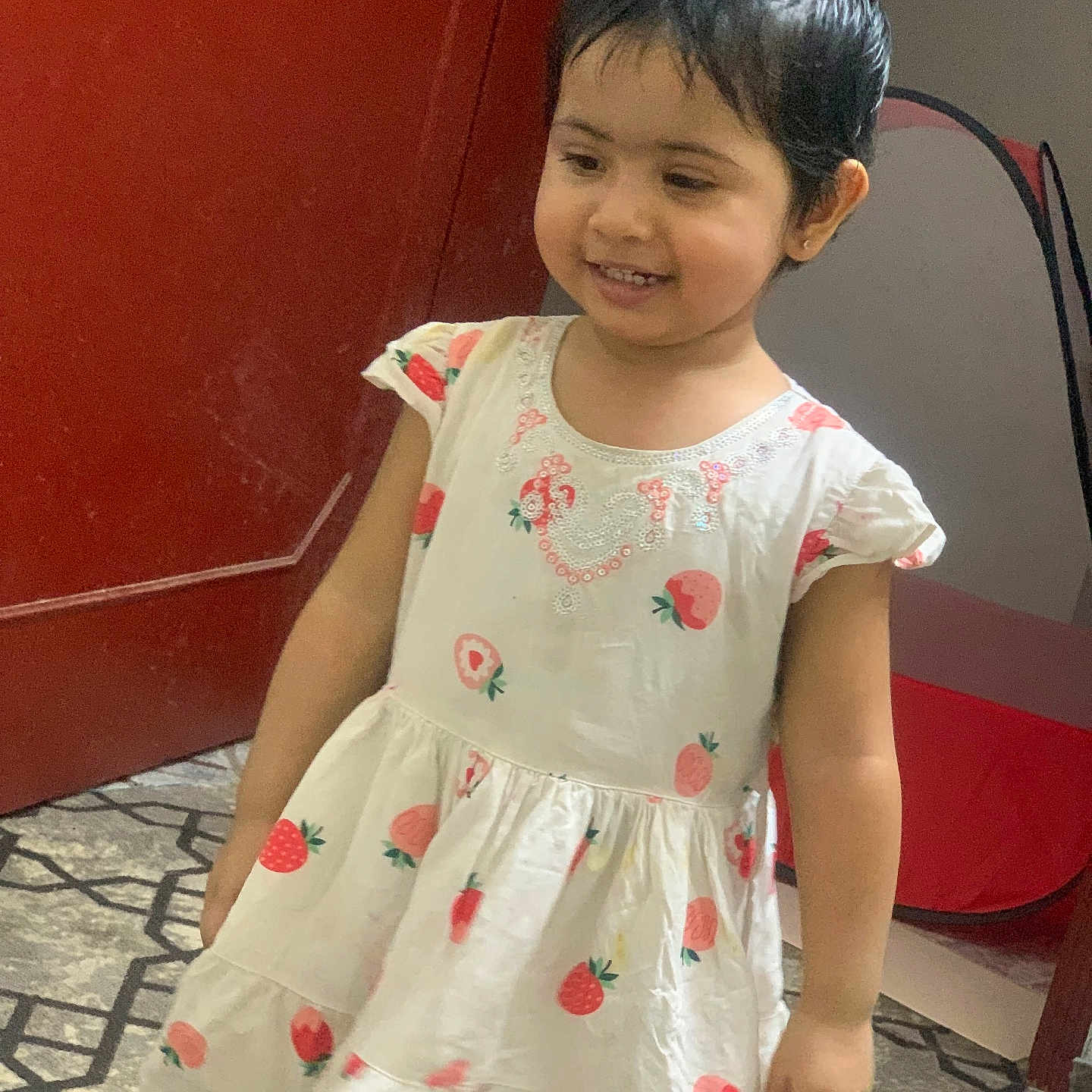 Fatma is registered to the contest to win money with this photo: carpet, child, cute, door, dress, floor, girl, happy, indoor, patterned_floor, person, portrait, red_door, short_hair, smile, standing, strawberry_print, toddler, white_dress, young_child