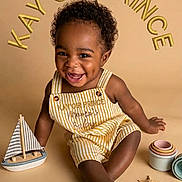 Kayoir joined the competition — help win amazing prizes! baby, child, toddler, smiling, happy, portrait, sitting, overalls, striped_clothing, curly_hair, dark_skin, toy_sailboat, sailboat, starfish, cups, beach_theme, studio, warm_lighting, text_overlay, fashion_photo