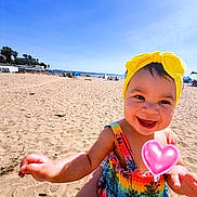 Gracie is registered to the contest to win money with this photo: beach, child, colorful_dress, cute, fun, happy, heart_sticker, holiday, outdoor, person, playful, portrait, sand, sky, smiling, summer, sunny, toddler, vacation, yellow_headband