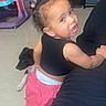 Sariah is registered to the contest to win money with this photo: toddler, child, puppy, black_top, pink_shorts, indoor, floor, toys, storage_boxes, curly_hair, leaning, looking_back, playful, pet, domestic_animal, home, furniture, cute, baby, person
