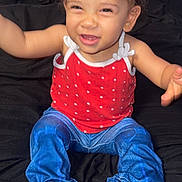 Sariah joined the competition — help win amazing prizes! toddler, child, smiling, curly_hair, red_tank_top, blue_pants, barefoot, bed, black_bedspread, indoor, happy, cute, playful, sitting, young_child, person, portrait, casual_clothing, baby, fun