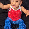 toddler, child, smiling, curly_hair, red_tank_top, blue_pants, barefoot, bed, black_bedspread, indoor, happy, cute, playful, sitting, young_child, person, portrait, casual_clothing, baby, fun