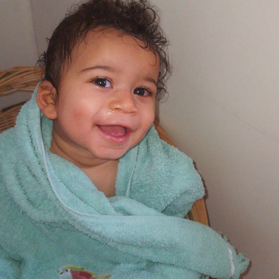 Thomas a rejoint le concours — aidez-le/la à gagner de superbes lots ! baby, basket, child, curly_hair, cute, expression, face, happy, indoors, infant, person, portrait, sitting, skin, smiling, towel, warm, wooden_floor, wrapped, young