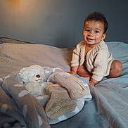 Thomas participe au concours pour gagner de l'argent avec cette photo : baby, child, smiling, knitted_sweater, bed, blanket, teddy_bear, socks, indoor, cozy, soft_light, person, furniture, cute, warm, portrait, happy, crawling, plush_toy, nursery