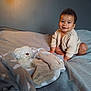 baby, child, smiling, knitted_sweater, bed, blanket, teddy_bear, socks, indoor, cozy, soft_light, person, furniture, cute, warm, portrait, happy, crawling, plush_toy, nursery