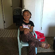 Zaniyah is registered to the contest to win money with this photo: child, girl, smiling, sitting, chair, indoor, carpet, clothing, hair_bow, leopard_print, sandal, toy_box, door, room, person, happy, portrait, casual, young, fashion