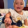 Hazel is registered to the contest to win money with this photo: baby, child, infant, smiling, happy, portrait, indoor, bedroom, blanket, sitting, headband, bow, dress, teddy_bear, toy, barefoot, hand, feet, furniture, close_up
