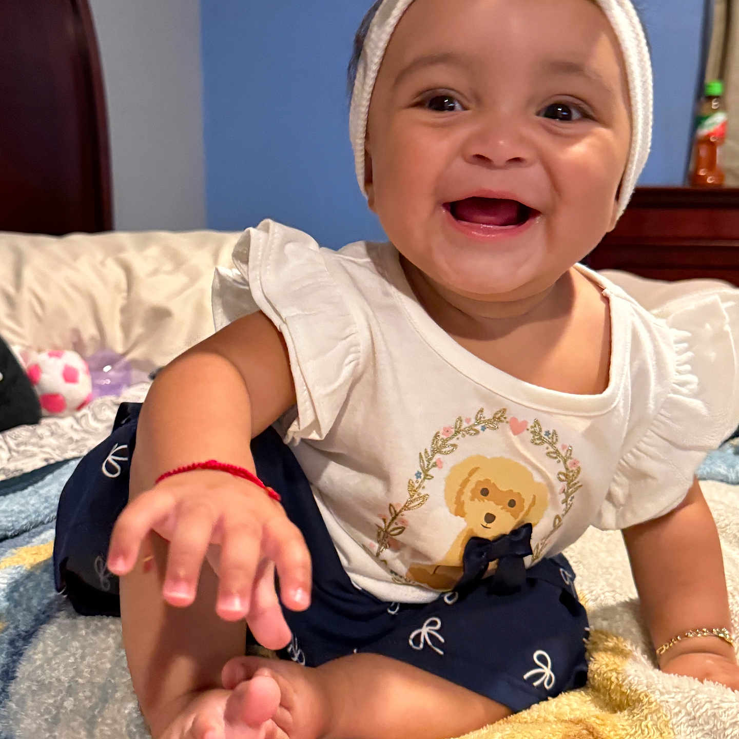 Hazel is registered to the contest to win money with this photo: baby, child, infant, smiling, happy, portrait, indoor, bedroom, blanket, sitting, headband, bow, dress, teddy_bear, toy, barefoot, hand, feet, furniture, close_up
