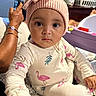baby, infant, child, portrait, sitting, indoors, pink_hat, bunny_hat, onesie, flamingo_pattern, wide_eyes, neutral_expression, toy, playpen, laundry_basket, adult_hand, smartphone, home, closeup, family