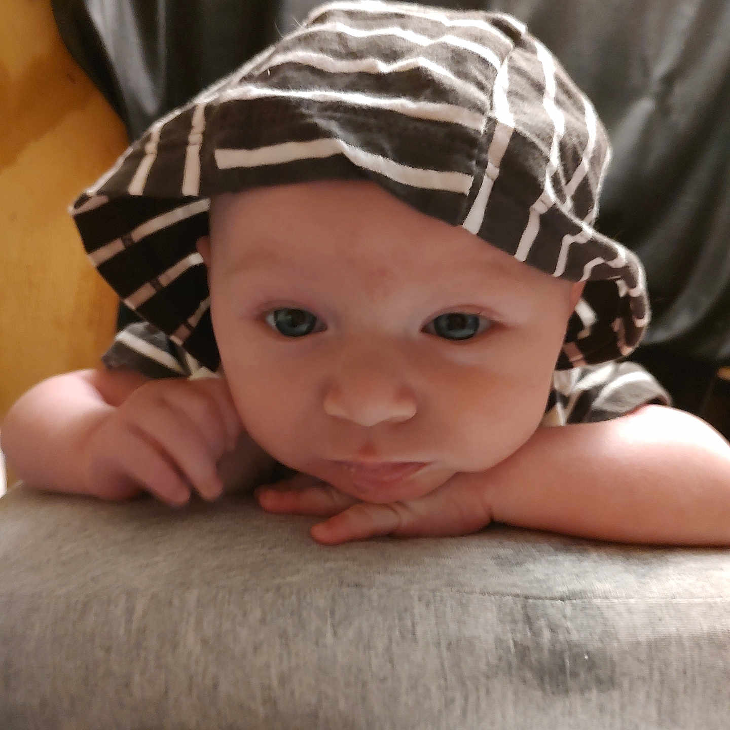 Luke is registered to the contest to win money with this photo: baby, baby_face, close_up, clothing, curious, cute, expression, eyes, face, hands, hat, headwear, indoor, infant, person, portrait, resting, soft_surface, striped_hat, young_child