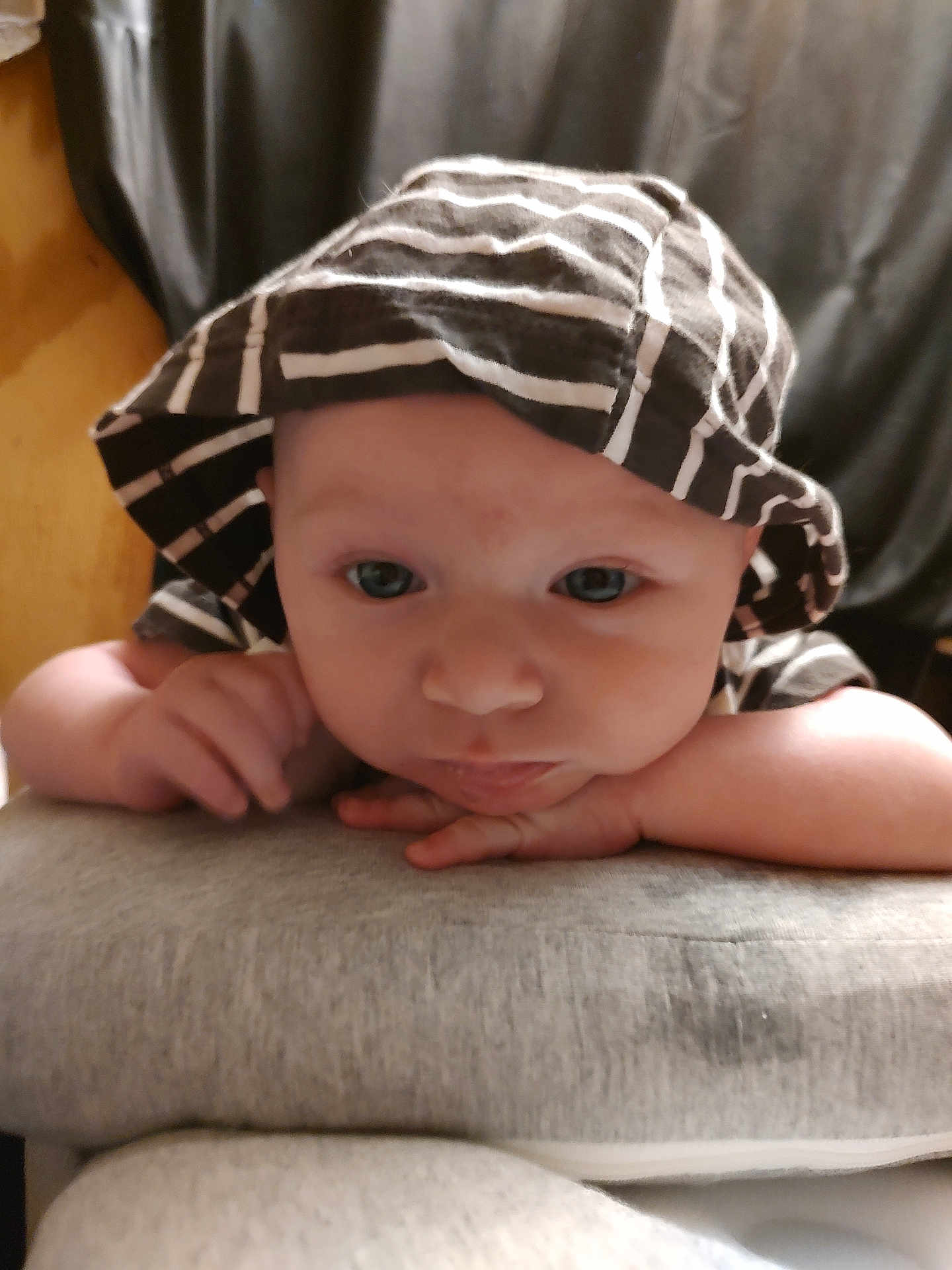 Luke is registered to the contest to win money with this photo: baby, infant, hat, striped_hat, face, eyes, hands, resting, indoor, soft_surface, curious, young_child, clothing, portrait, close_up, headwear, person, cute, baby_face, expression