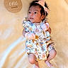Areli is registered to the contest to win money with this photo: baby, infant, one_month, floral_outfit, pink_bow, mittens, blanket, wooden_plaque, milestone, cute, newborn, portrait, lying_down, soft_light, indoors, child, small_feet, curious_expression, headband, baby_clothes