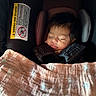 baby, sleeping, car_seat, blanket, infant, child, face, head, hair, safety_harness, pink_blanket, patterned_blanket, cozy, indoor, closeup, peaceful, resting, cute, newborn, seat